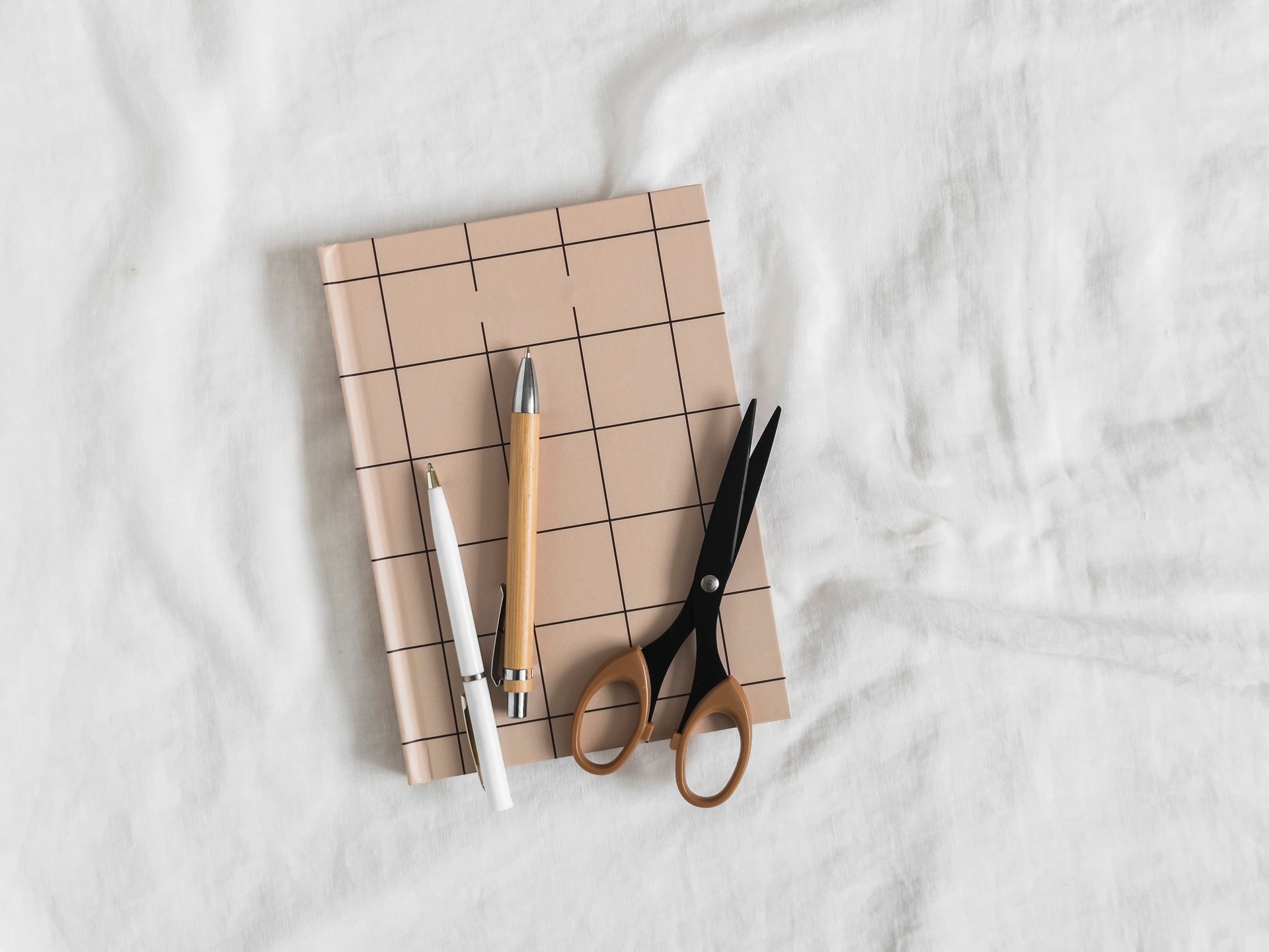 Minimalism style women's accessories - notebooks, pens, scissors on a light background, top view